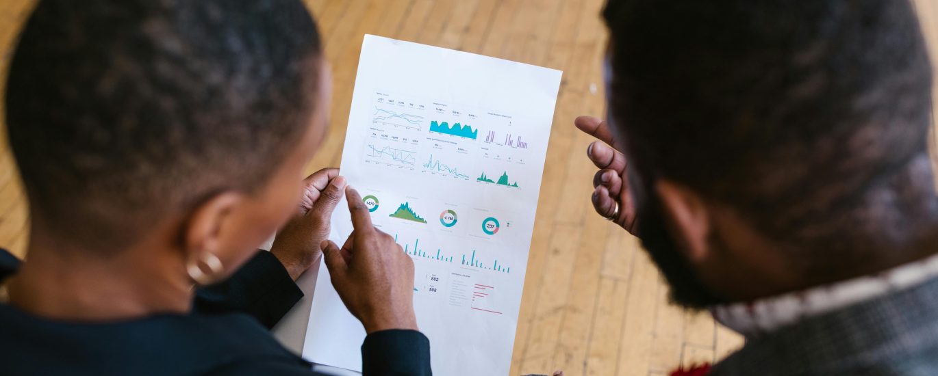 Two business colleagues examining a document with charts in an office setting.